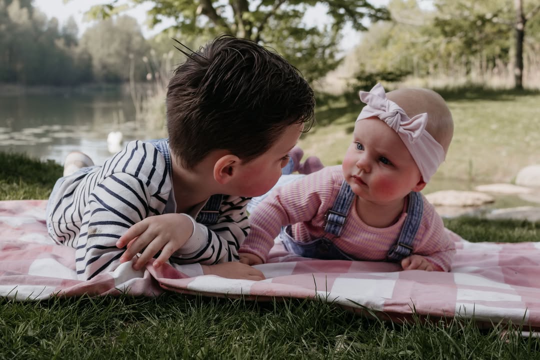 Grote broer kijkt naar zijn babyzusje op een picknickkleed