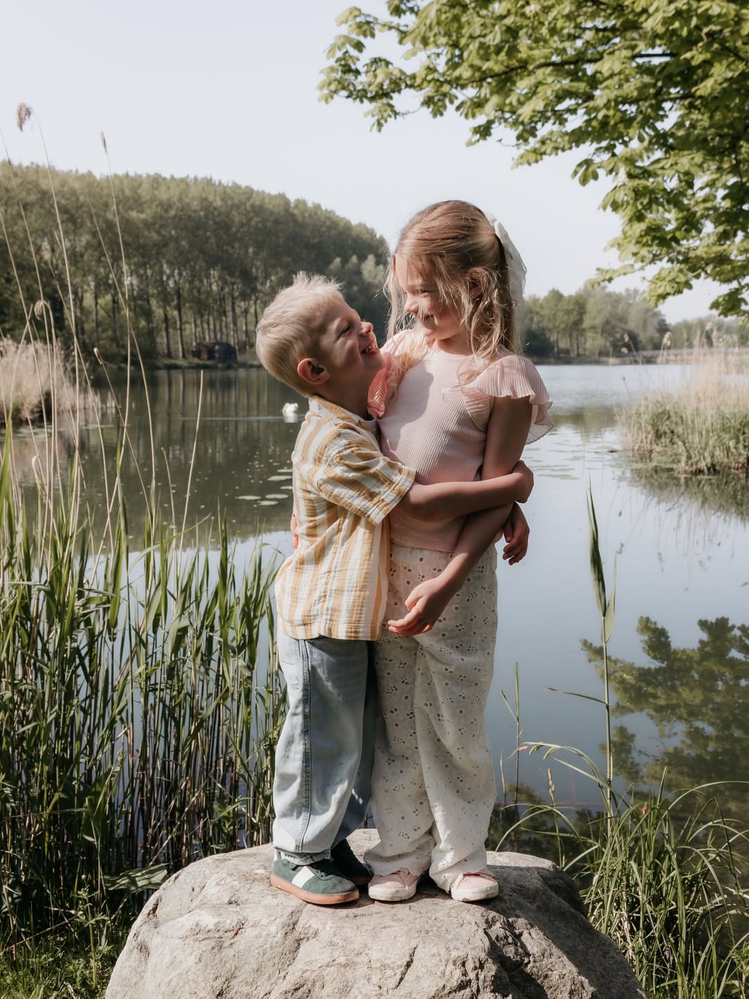 Broer en zus omhelzen elkaar lachend op een rots aan het water