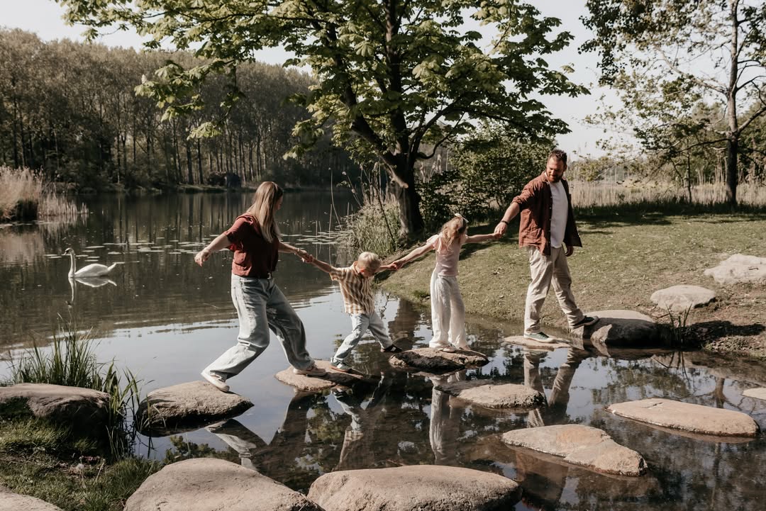 Gezin loopt hand in hand over stapstenen door het water