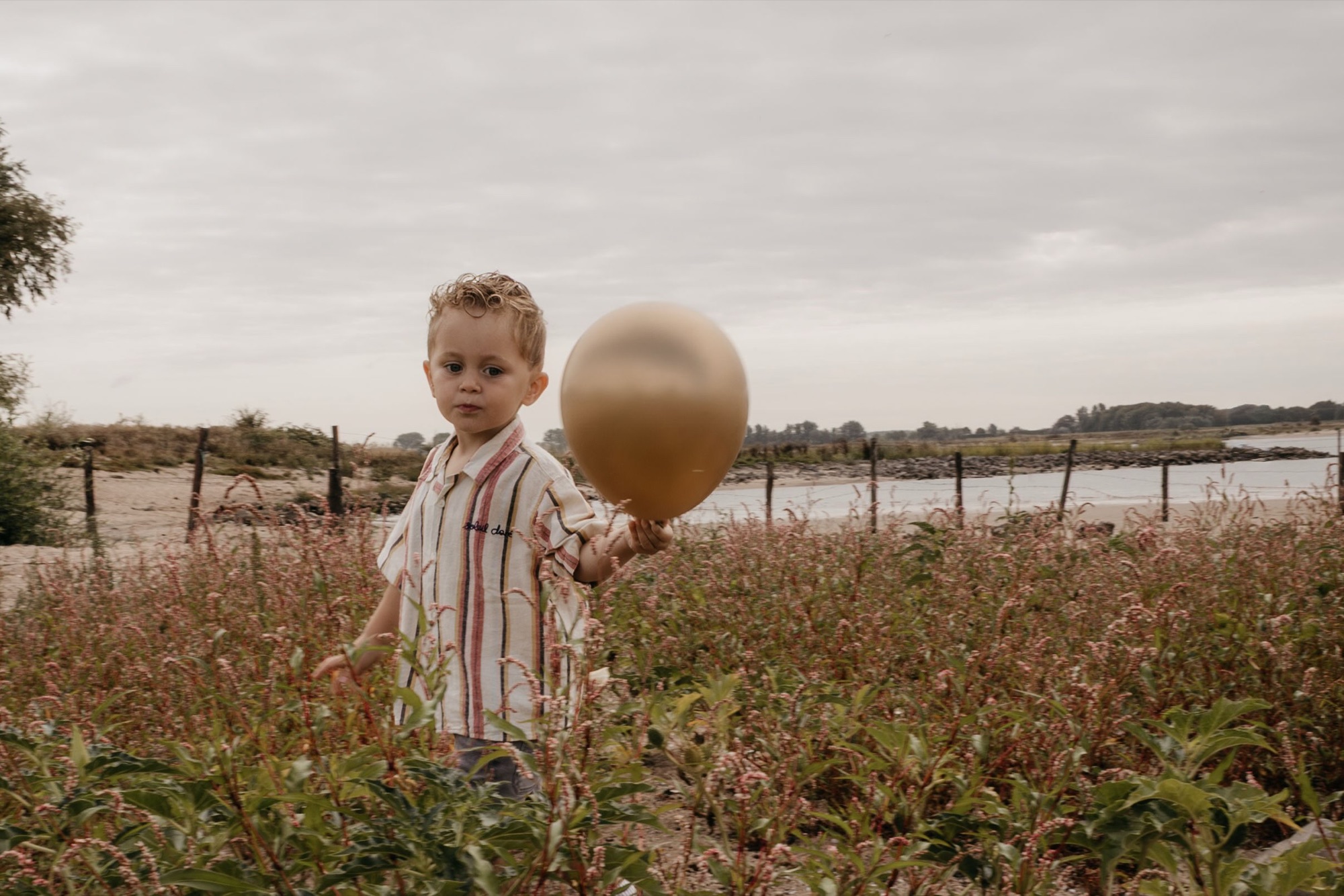 Jongetje met een gouden ballon in een veld aan de rivier
