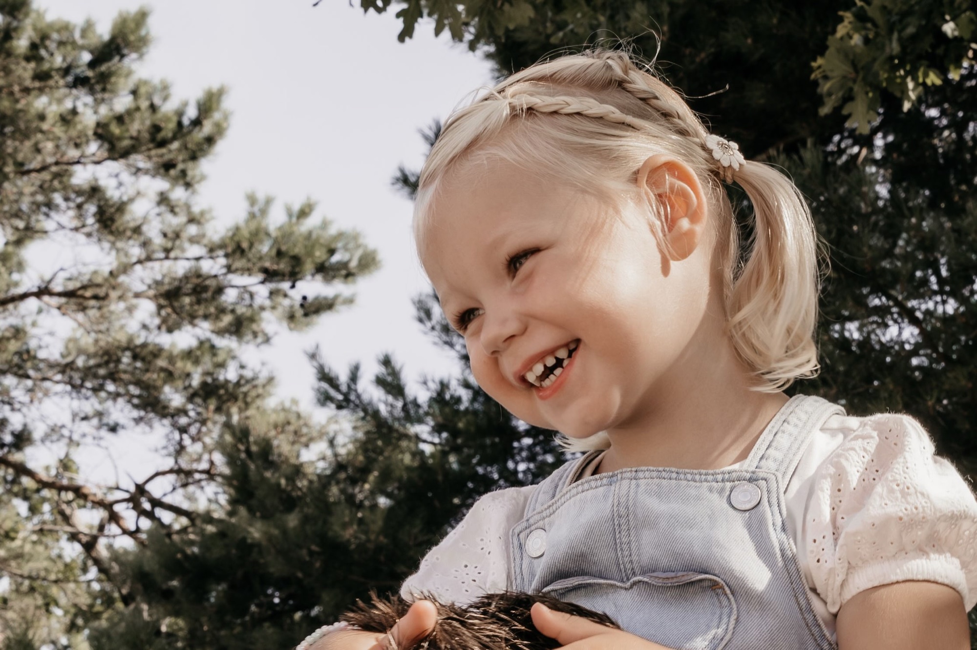 Lachend meisje met vlechtjes in het zonlicht onder de bomen