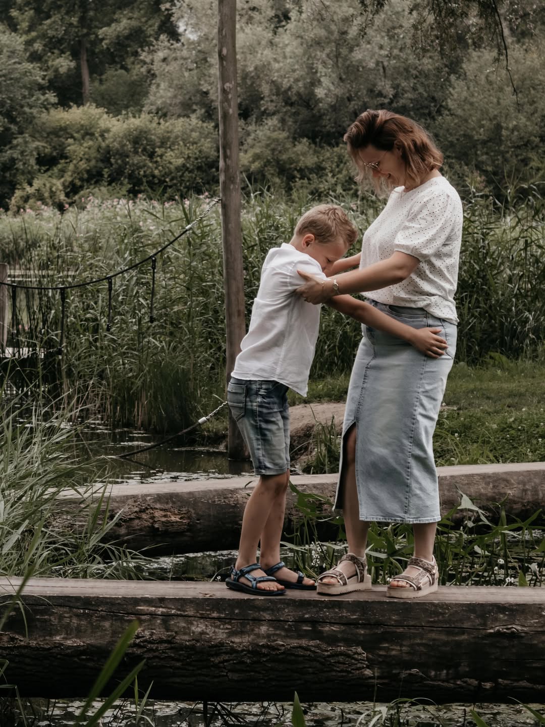 Moeder houdt haar zoon vast op een boomstam boven het water