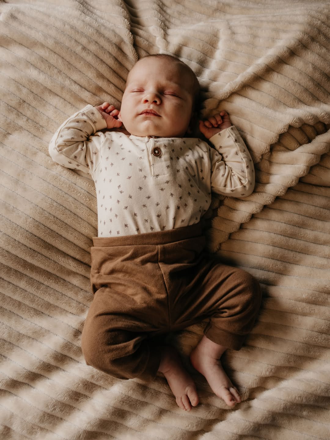 Pasgeboren baby slaapt met de armpjes omhoog op een zachte deken