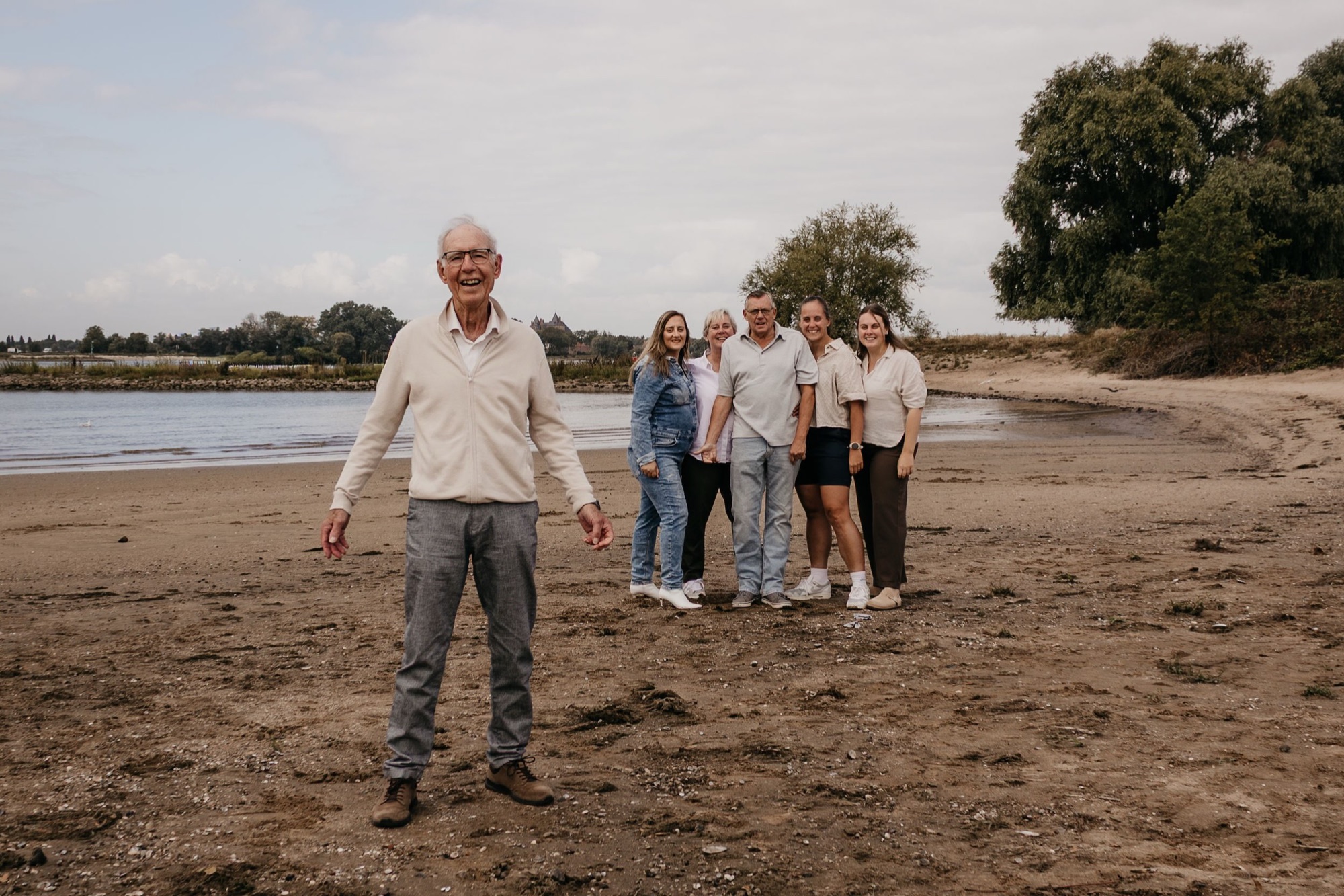 Opa staat vooraan op het strand, zijn familie achter hem