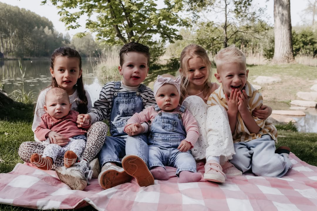 Zes kinderen op een geruit picknickkleed aan het water