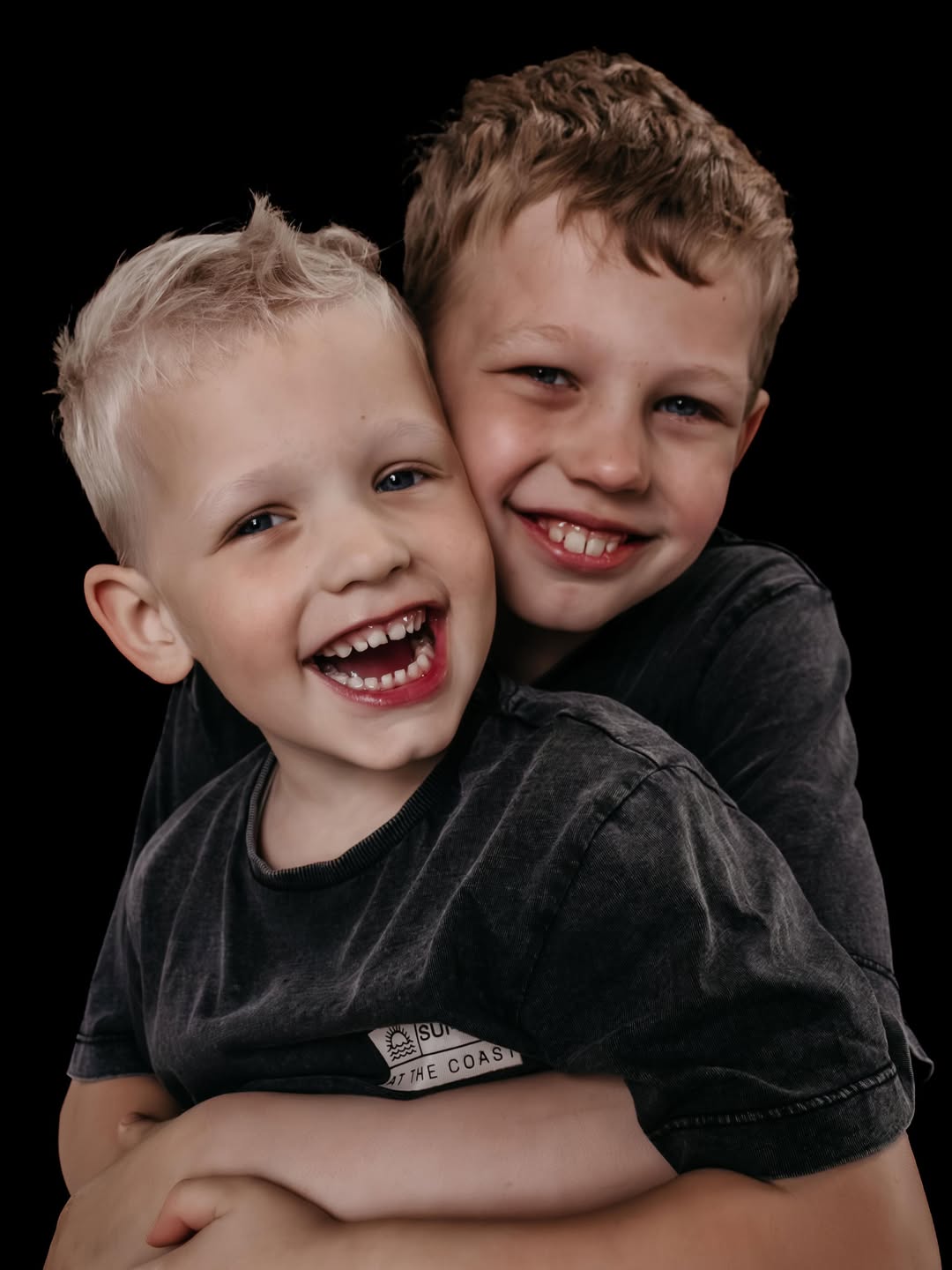 Twee broers lachen dicht tegen elkaar tegen een zwarte achtergrond