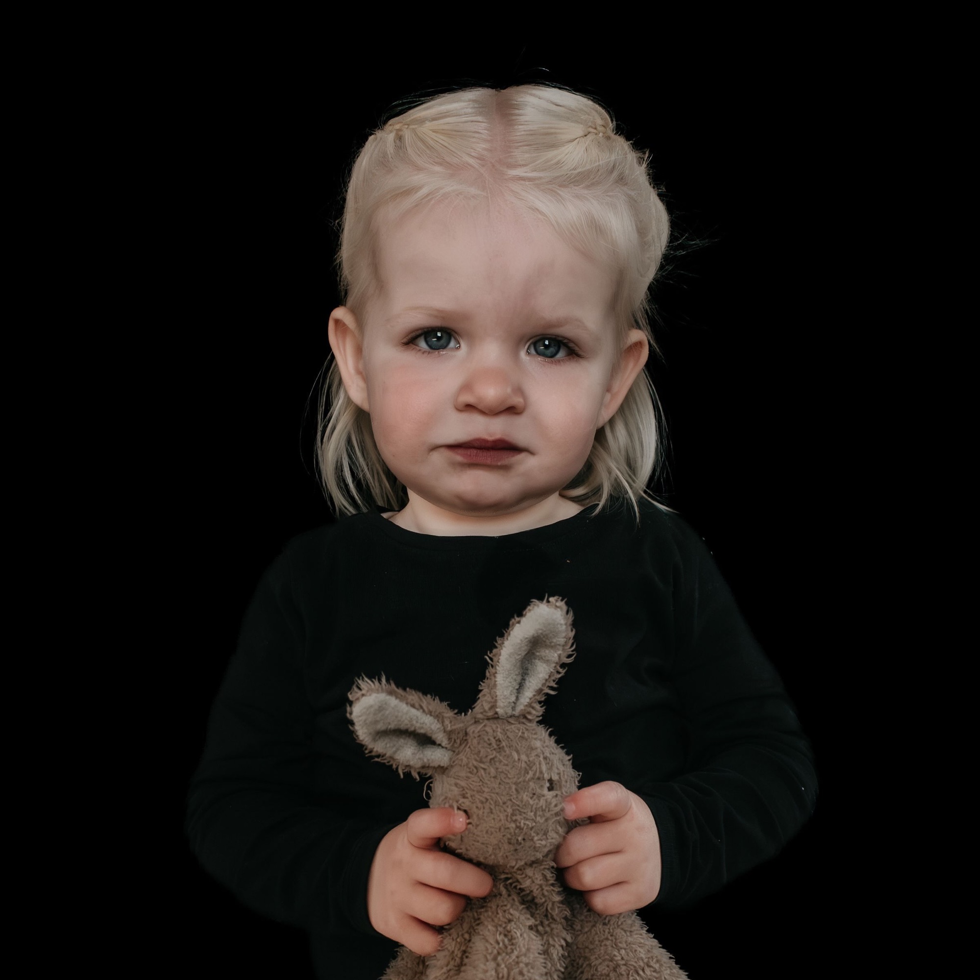 Peuter met een knuffelkonijn tegen een zwarte achtergrond