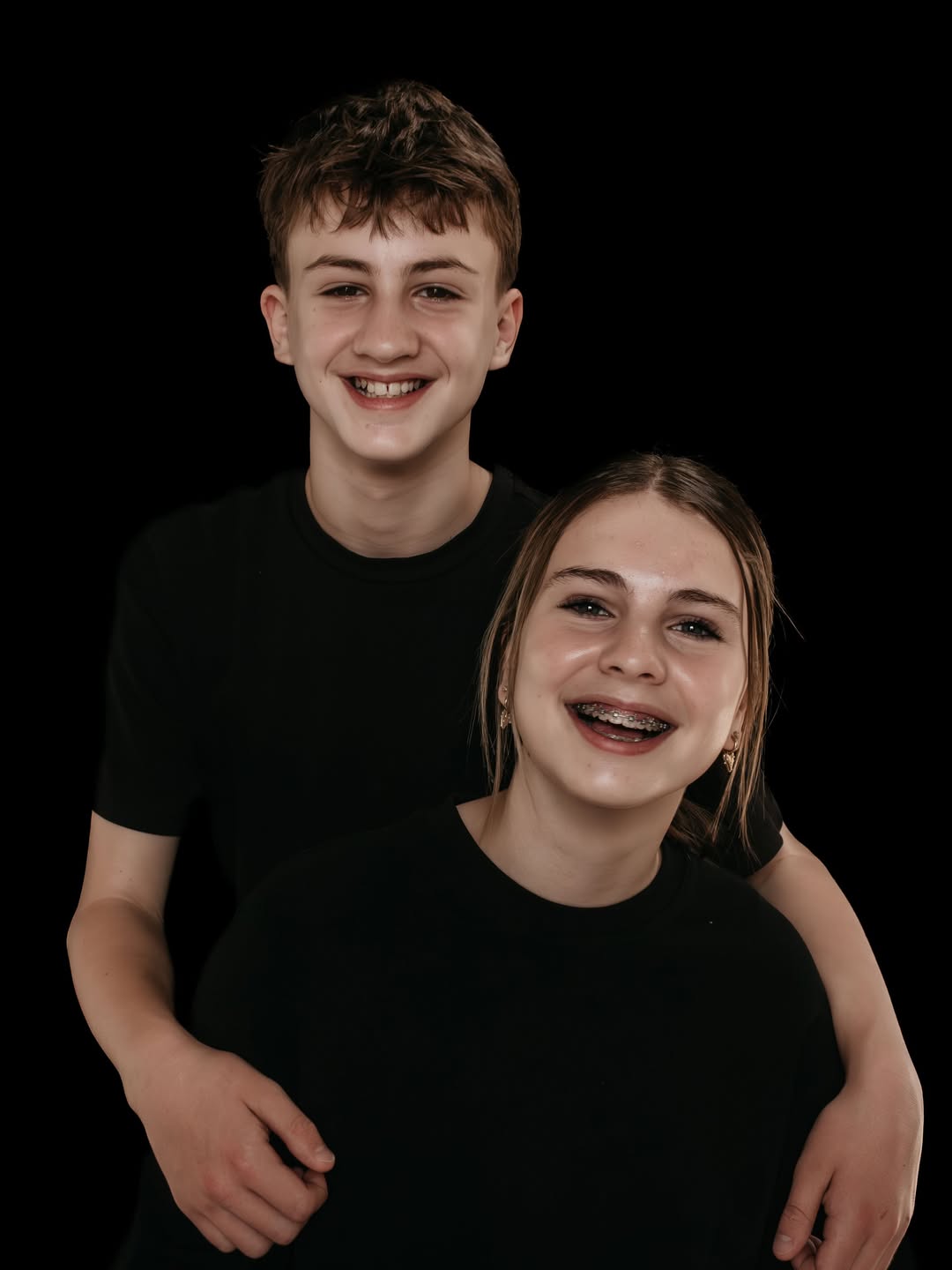 Broer en zus in de tienerleeftijd lachen tegen een zwarte achtergrond