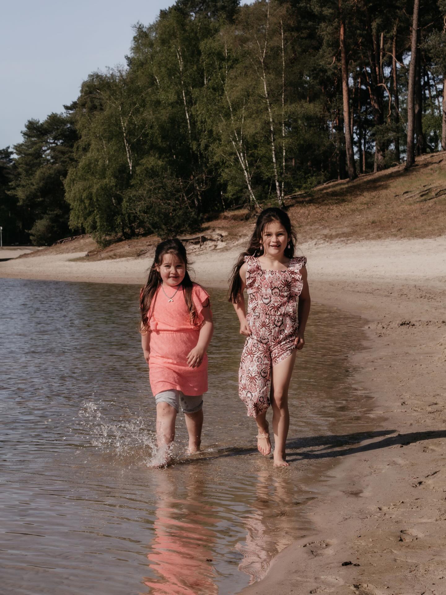 Twee zusjes rennen door het ondiepe water langs het strand